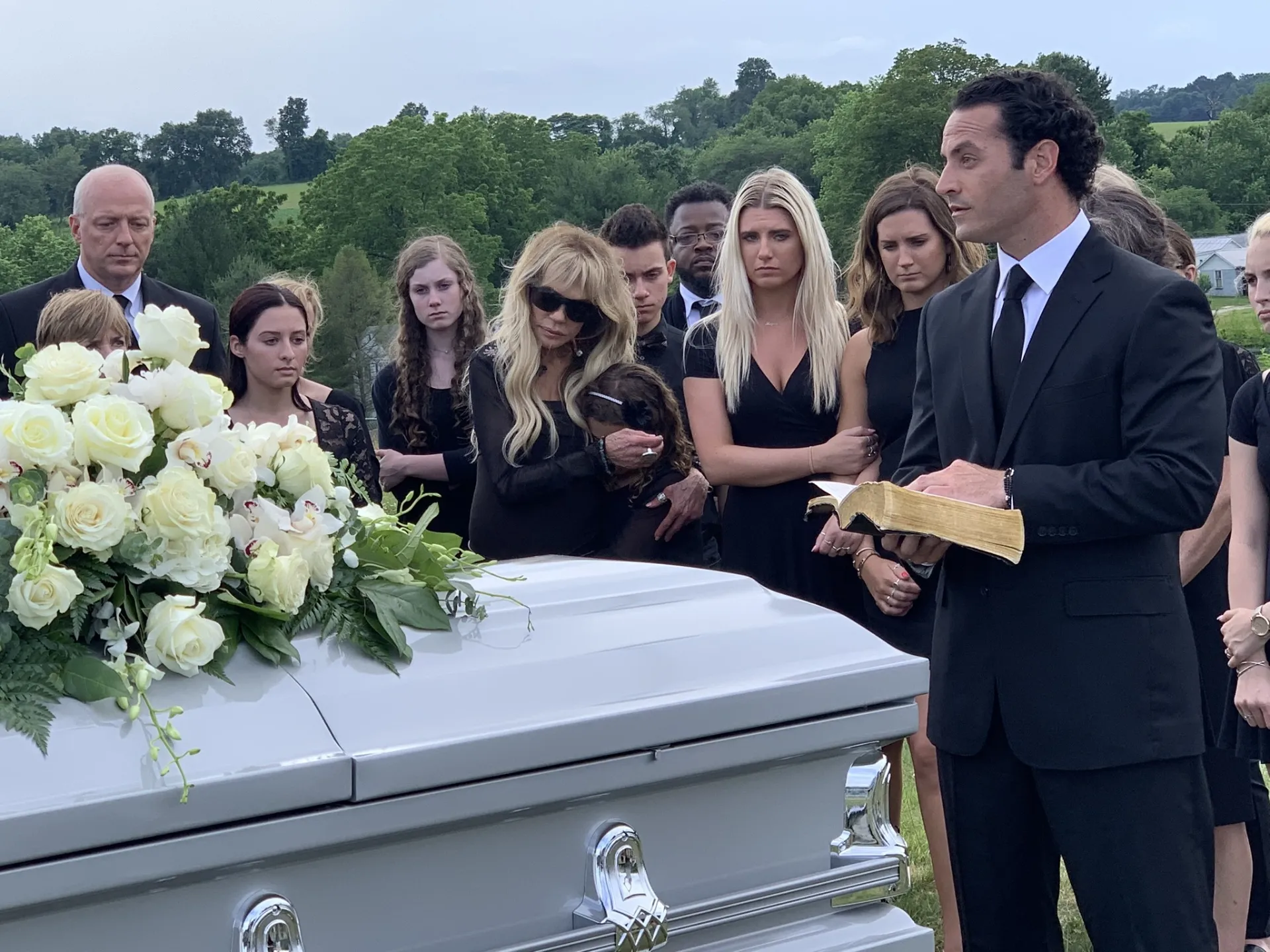 Family gathered at a graveside funeral service with white casket and flowers